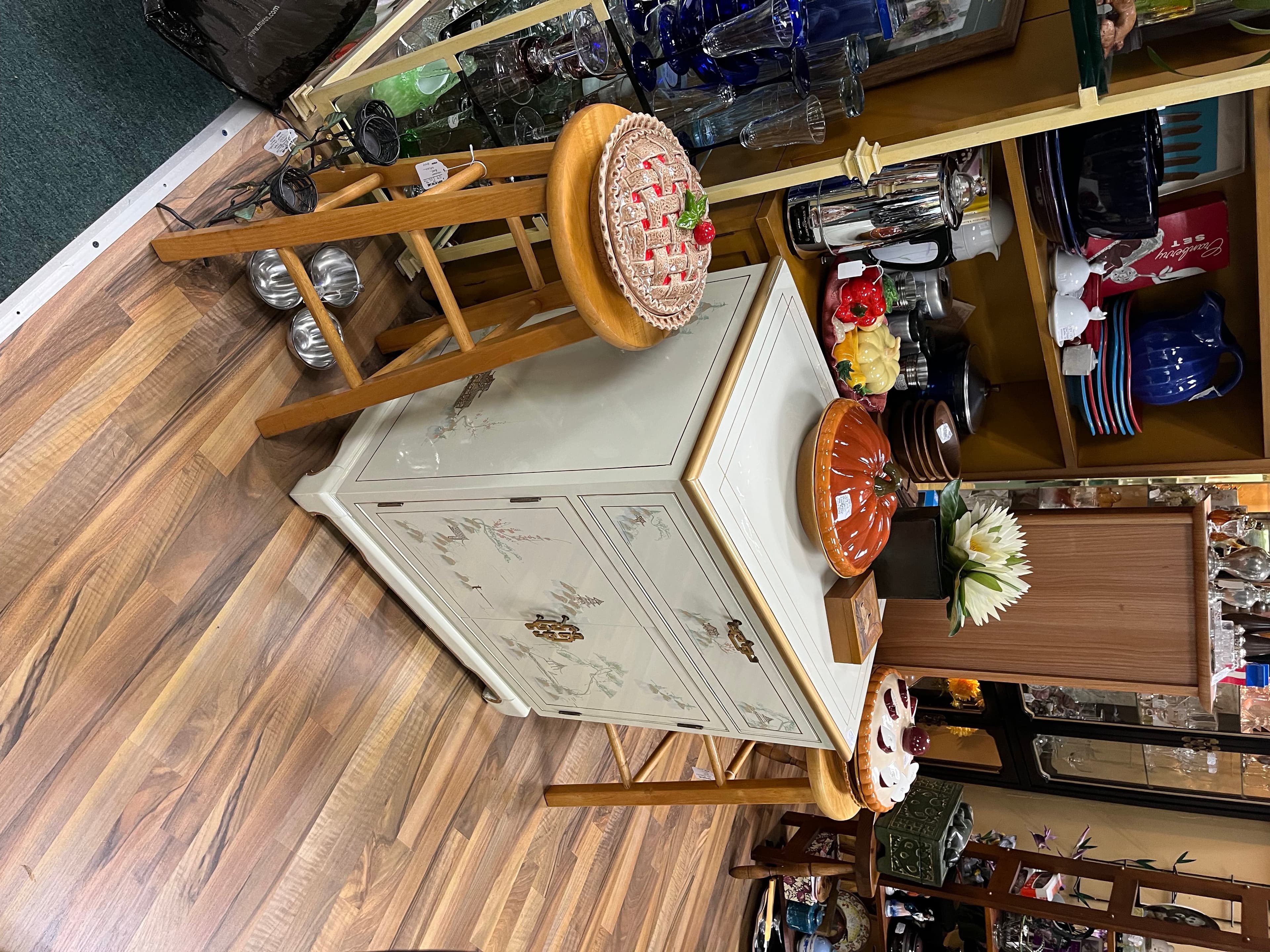 A cream hand-painted cabinet with cherry blossom motif, beside a woven stool with a strawberry cushion.