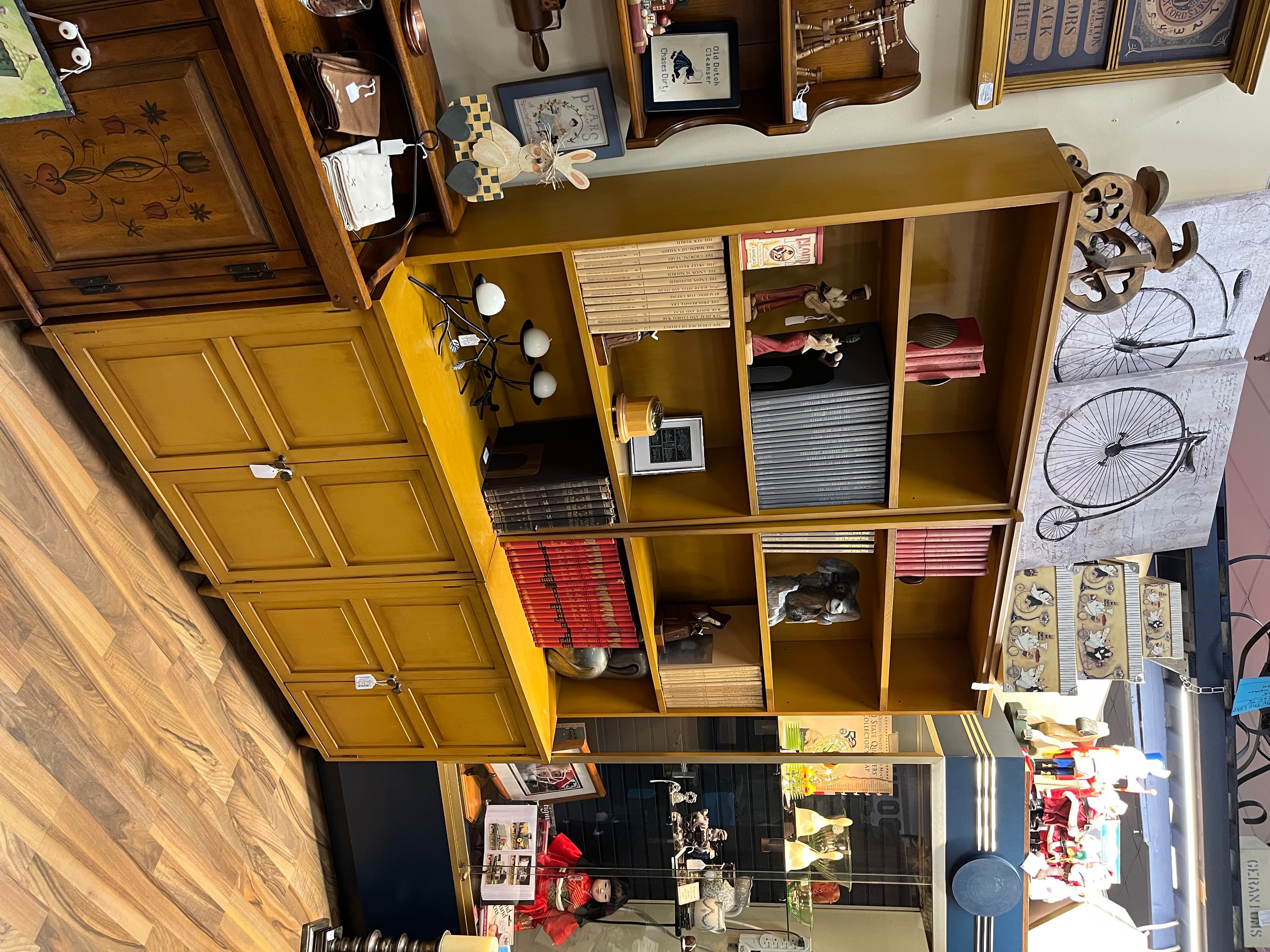 A mustard-yellow cubby shelf full of small books and collected oddities, with cabinet doors below.
